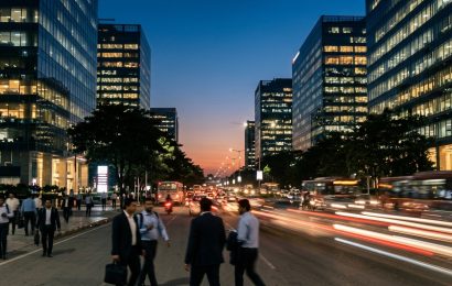Long exposure of traffic light trails on a boulevard below office towers at dusk in India